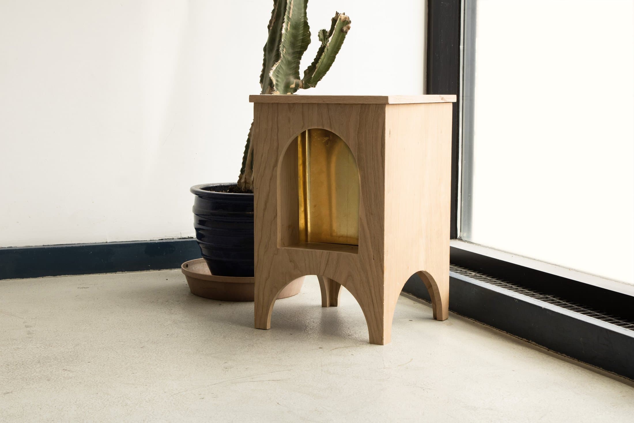 The cherry wood side table from the collection, next to a potted cactus